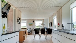 Una cocina moderna con comedor, piso de madera y ventanas amplias.