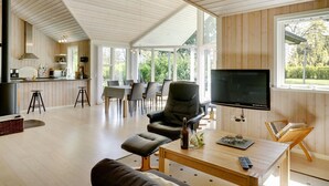 Ein geräumiger Wohnbereich mit großem Fernseher, Holzboden und Essbereich mit Tageslicht.