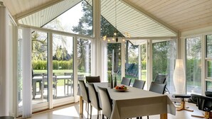 Ein geräumiger Essbereich mit großem Tisch, Stühlen und Blick auf einen Garten durch große Fenster.