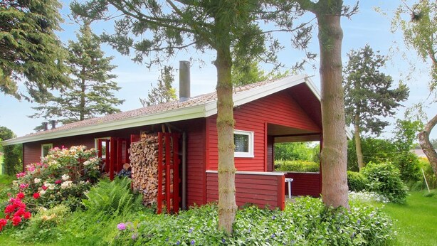 Une maison rouge avec un toit en pente, entourée d’une végétation luxuriante et de plantes en fleurs.