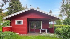 Une cabane en bois rouge avec un porche couvert, une petite table et une porte donnant sur un espace clos.