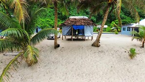 A thatched-roof hut with a blue tarp, surrounded by palm trees and a sandy beach. - Jaymy Beach Fales (Saleapaga)