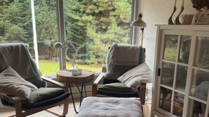 A cozy seating area with two chairs and a small table, a lamp, and a view of a forest through a glass door.