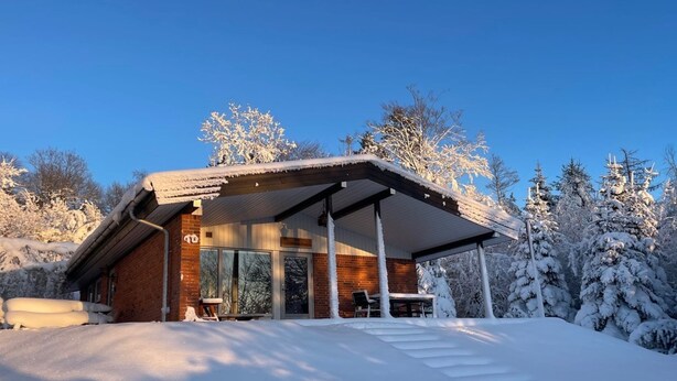 A modern house with a covered patio, brick walls, and a snowy landscape.