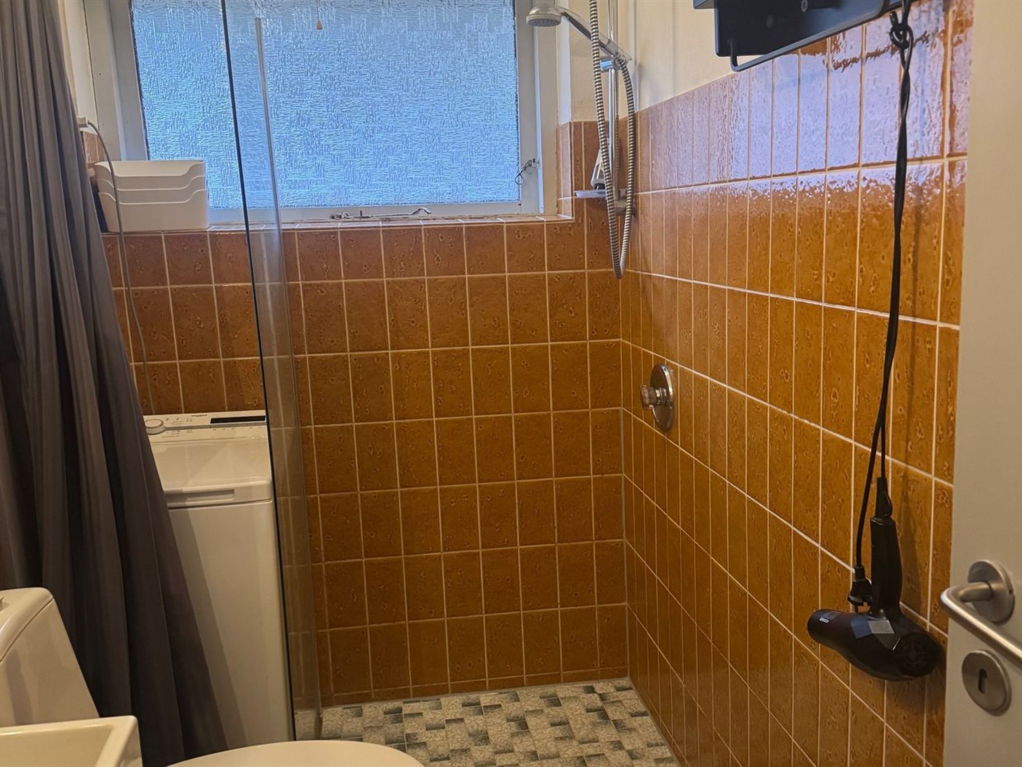 A small bathroom with a shower, tiled walls, a window, and a toilet.