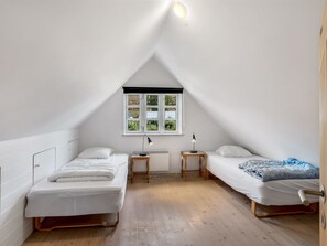 Een kleine, driehoekige zolderkamer met twee bedden, een raam en een radiator.