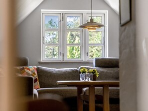 Une pièce avec une fenêtre, un canapé, une table et un luminaire suspendu.