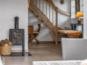 A cozy room with a wood-burning stove, a dining table, and a staircase.