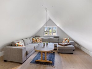 Een moderne loft slaapkamer met een groot raam, een grijze modulaire bank, een ronde salontafel en een klein bijzettafeltje.