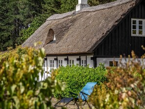 A thatched-roof house with a white exterior and a black door, surrounded by greenery.