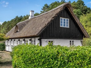 Een huis met een rieten dak en witte buitenkant, omringd door weelderige begroeiing.