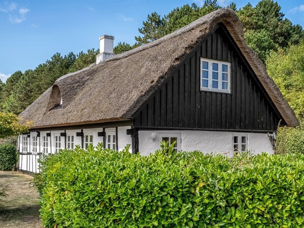 A traditional thatched-roof house with a white exterior, surrounded by lush greenery.