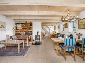 Un intérieur chaleureux avec un plafond en bois, une cheminée, un coin repas avec des chaises à rayures et une bibliothèque.
