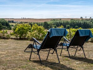 Deux chaises d’extérieur recouvertes de housses bleues, placées sur un terrain herbeux, avec un vignoble et des collines en arrière-plan.
