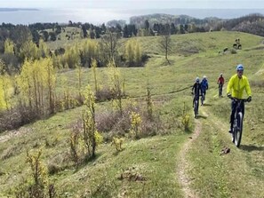 A group of cyclists on a grassy trail with trees and hills in the background.