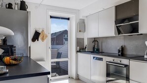 Et moderne køkken med hvide skabe, en sort bordplade og en indbygget ovn. Der er et vindue med udsigt, og en dør til en patio.