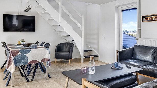 En moderne stue med trappe, spiseområde med bord og stole, samt en sofa.