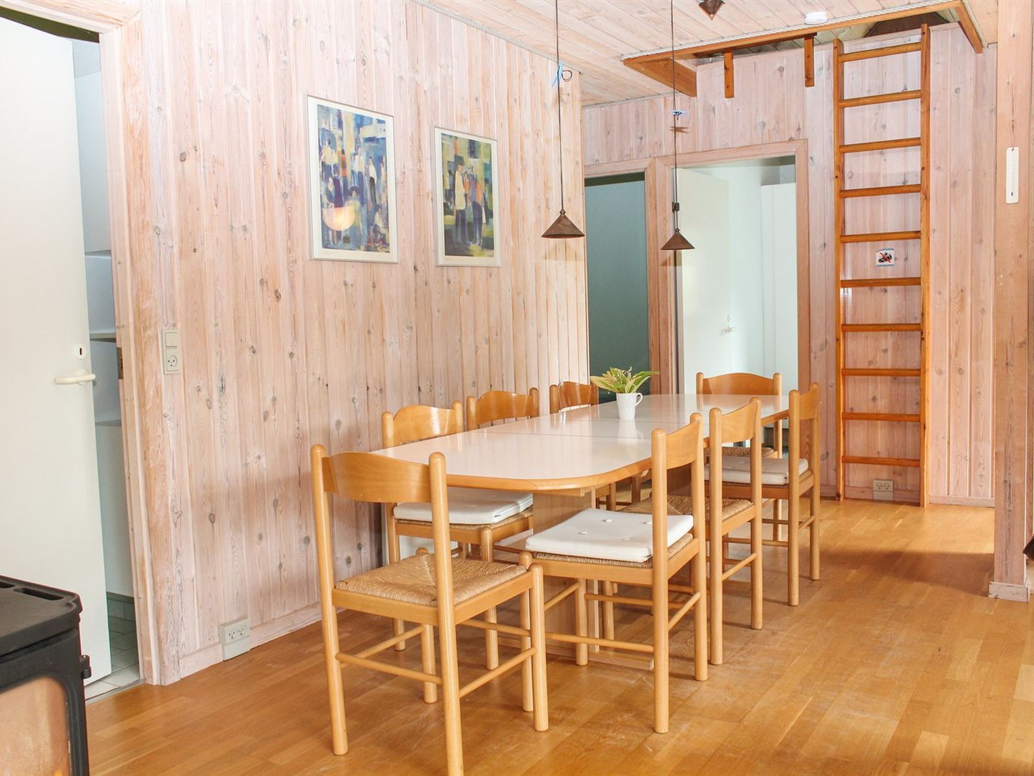 Un coin repas avec une table et des chaises en bois, une plante posée sur la table et une échelle en bois appuyée contre le mur.