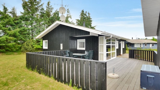 Une cabane avec une terrasse, une antenne parabolique et une cour clôturée.