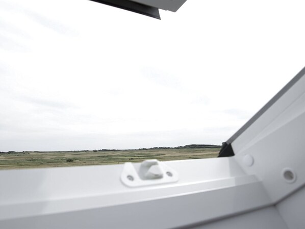 A view from inside a vehicle with a white interior, looking out at a flat landscape with a cloudy sky.