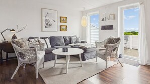 A modern living room with a grey sofa, two wicker chairs, a round coffee table, and a large window with a view.