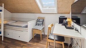 A dorm-style room with a loft bed, a desk with a chair, a computer, and a window.