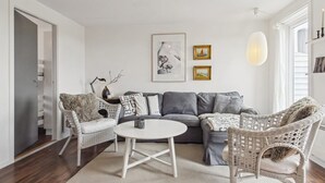 A modern living room with a grey sofa, wicker chairs, a white coffee table, and a large rug.