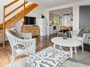 A modern living room with wicker furniture, a flat-screen TV, and a kitchen in the background.
