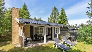 Ein Haus mit einer Terrassenanlage, einem Grill und Gartenmöbeln.