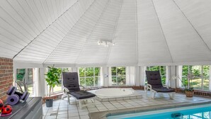 Een zonnig binnenzwembad met een bakstenen muur, betegelde vloer en ligbedden.