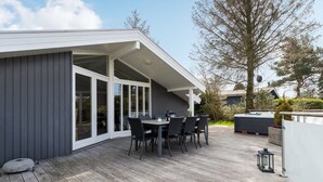 A modern outdoor patio with a dining area, large sliding glass doors, and a hot tub. - "Justiina" - 800m from the sea by Interhome (Væggerløse)