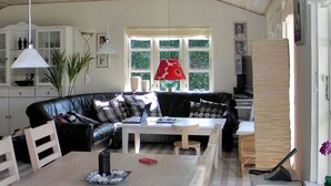 A cozy living room with a black leather sofa, a wooden coffee table, and a dining table. There is a window with a view of greenery outside. - "Nitis" - 200m from the sea by Interhome (Væggerløse)