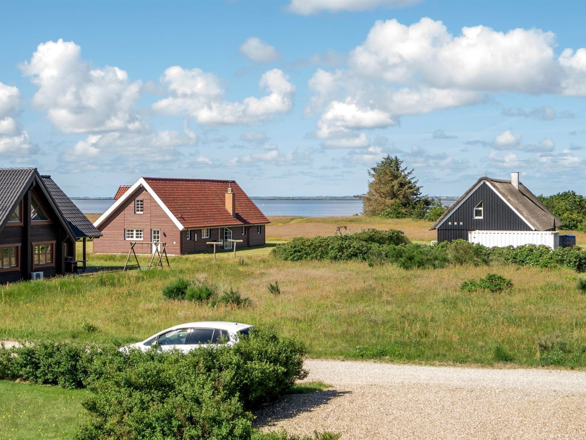 Une propriété située sur la côte, comprenant trois maisons, une allée en gravier et une voiture garée au premier plan.