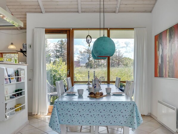 A dining area with a table set for four, a hanging pendant light, and a view of the outdoors through large windows.