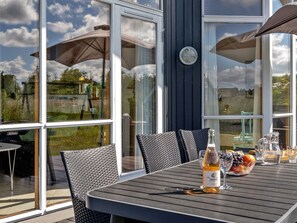 An outdoor dining area with a table, chairs, umbrellas, and a bottle of wine.