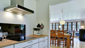 A modern kitchen with a built-in stove, white cabinets, and a dining area with wooden chairs and a table. - "Satzur" - 800m from the sea by Interhome (Blåvand)