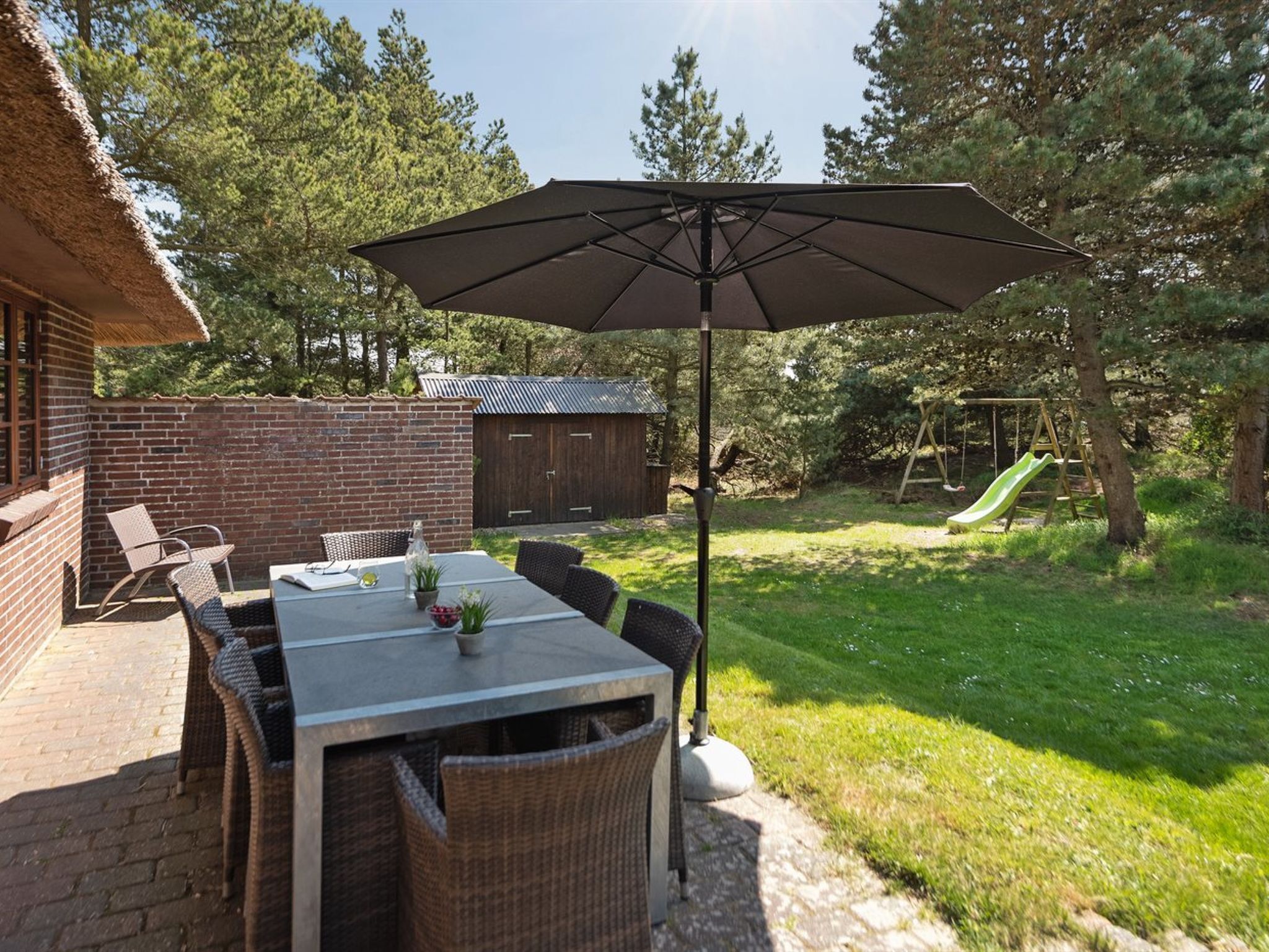 Eine Terrasse mit Tisch, Stühlen und einem Sonnenschirm, im Hintergrund eine Rutsche.