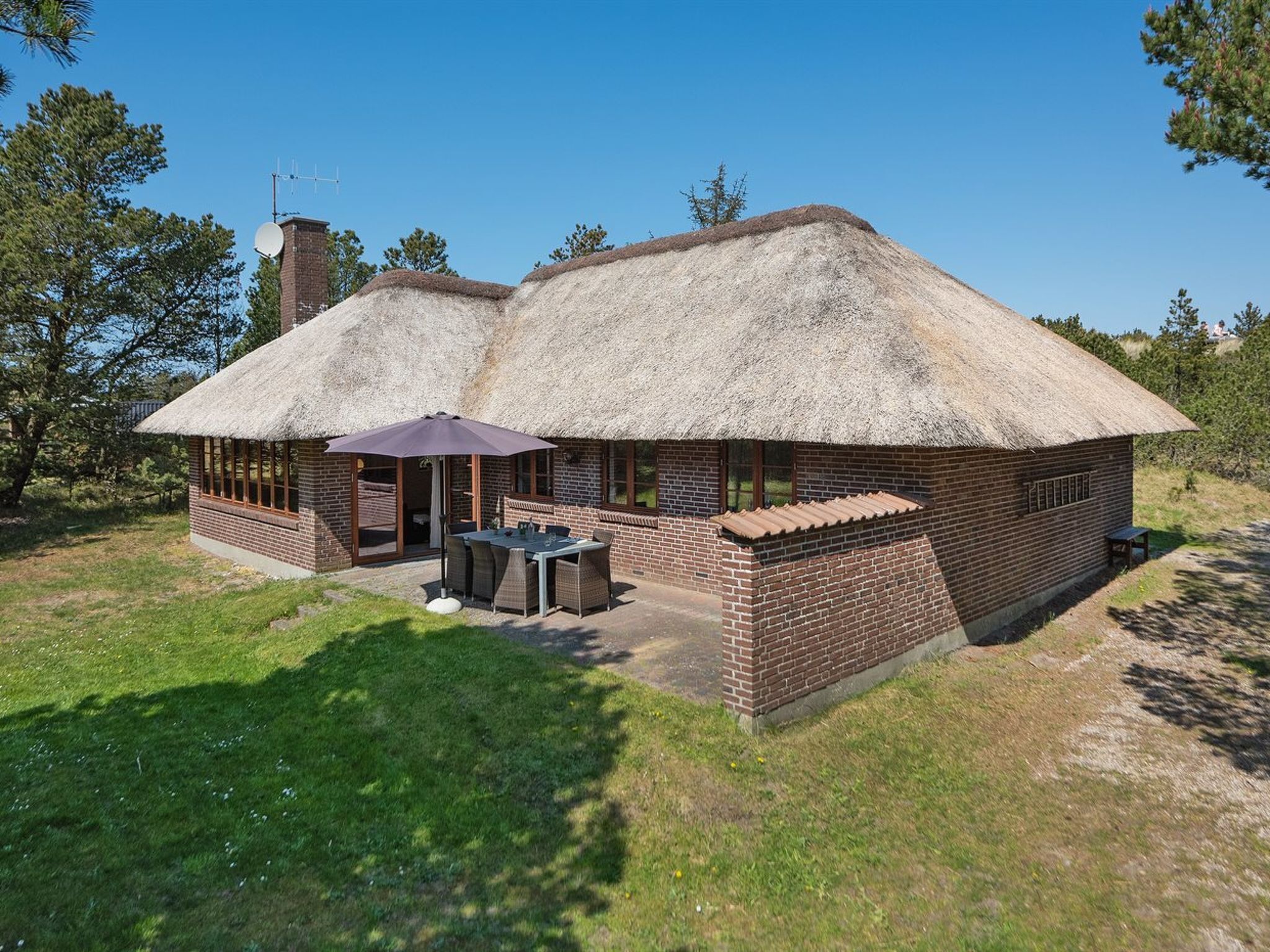 A thatched-roof cottage with a patio, brick walls, and a satellite dish.