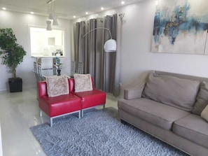 A modern living room with a red sofa, a beige sofa, a grey shag rug, and a dining area with a table and chairs.