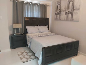 A bedroom with a bed, nightstands, a lamp, a rug, and a painting on the wall.