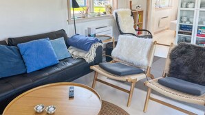 Ein Wohnzimmer mit einem schwarzen Ledersofa, blauen Kissen, einem Korbstuhl mit einer weißen Felldecke und einem Holztisch.