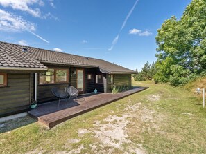 Et moderne hus med en træterrasse, en overdækket veranda og en græsplæne.