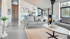 Een moderne woonkamer met een open haard, grijze banken en een groot raam.