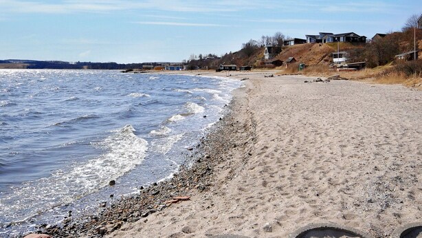 A beach with a sandy shore, a rocky beach area, and houses in the background. - "Aliza" - 300m to the fjord by Interhome (Roslev)
