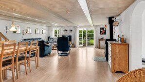 A spacious living area with wooden flooring, a sofa, chairs, a dining table, and a kitchen area with a wooden cabinet and a clock on the wall. - "Aliza" - 300m to the fjord by Interhome (Roslev)