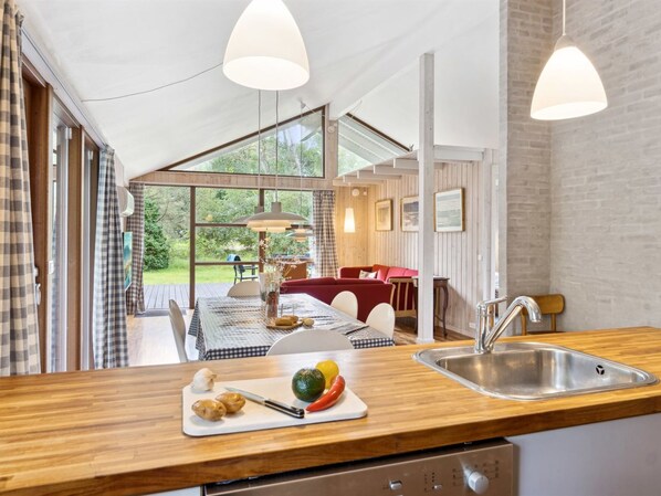 A modern kitchen with wooden countertops, a sink, and a dining area with a red sofa and table.