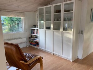 Una habitación con una silla de madera, un armario blanco con puertas de cristal y una ventana que da a zonas verdes.
