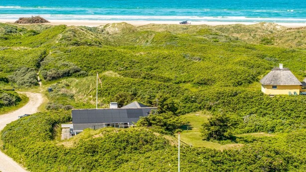 Een kustlandschap met een modern huis, een pad en een strand.