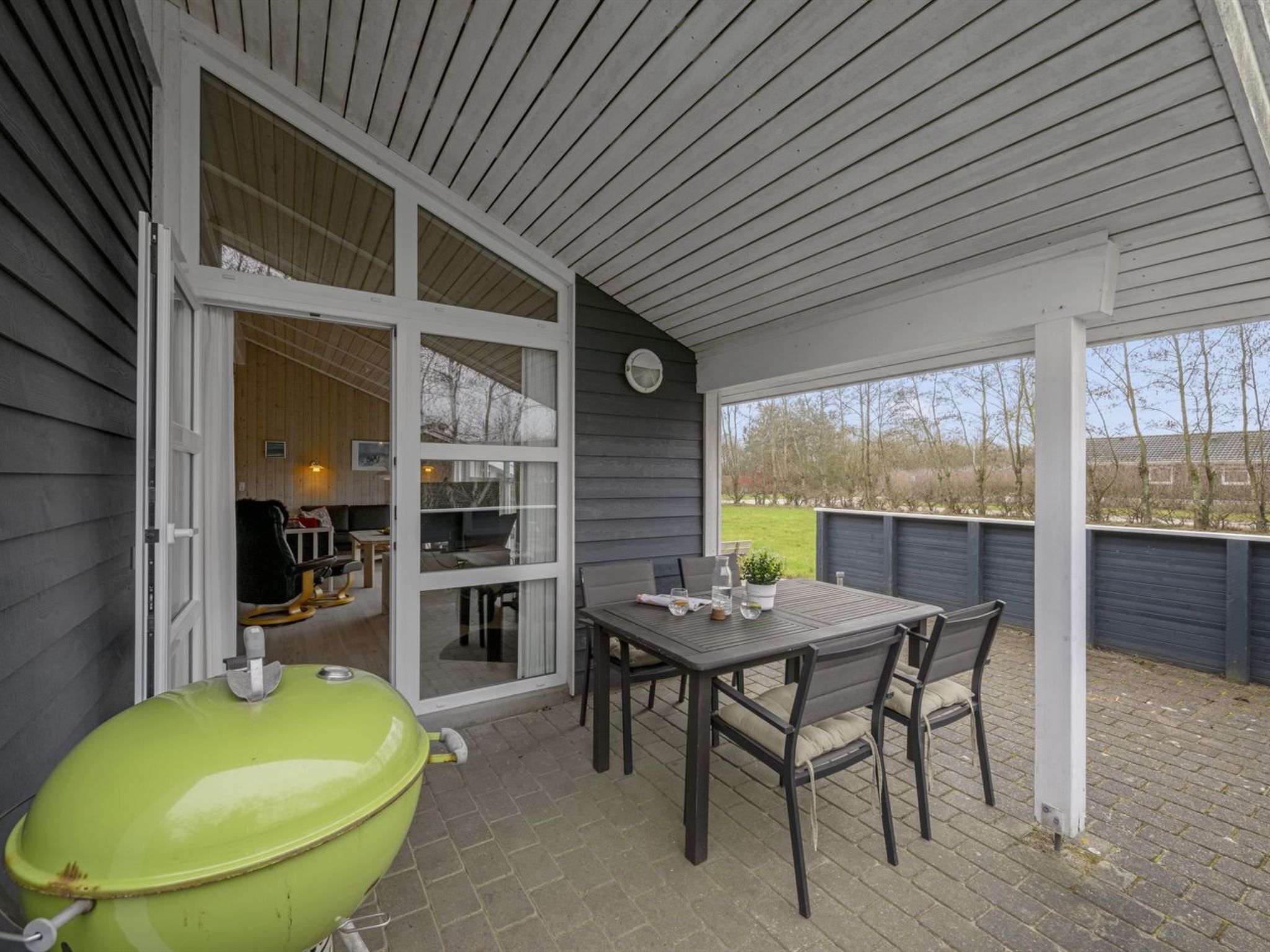 Une terrasse extérieure avec une table et des chaises, un barbecue vert et une vue sur les environs.