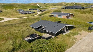 Un quartier résidentiel moderne avec des maisons construites sur des collines verdoyantes, un ciel dégagé et des éoliennes en arrière-plan.